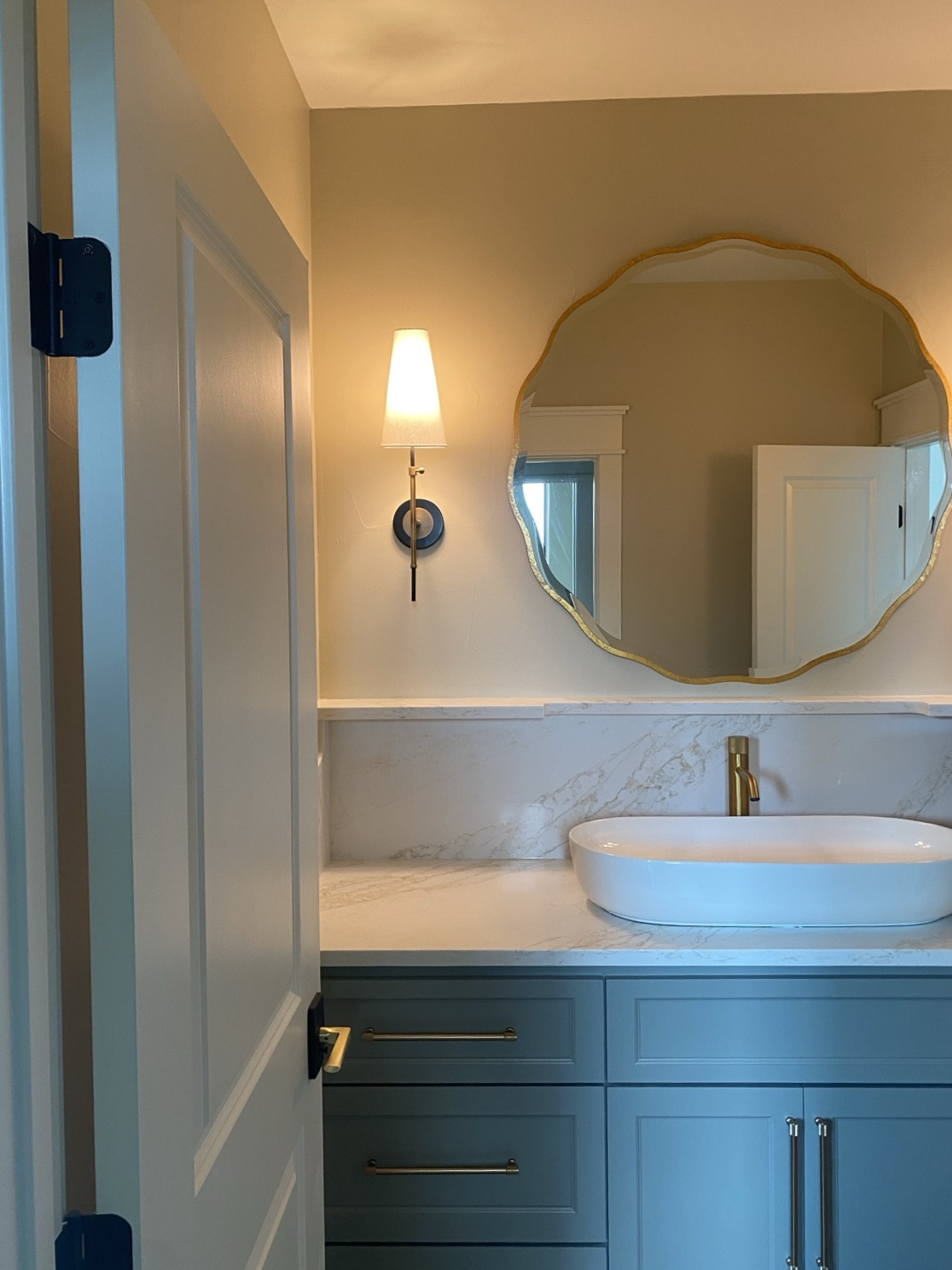 Completed bathroom vanity with quartz surfaces, custom cabinetry, sculpted mirror, and wall sconce